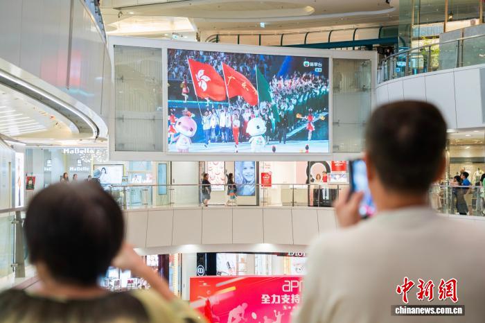 11月9日晚，香港市民在觀塘的一家商場內通過大屏幕觀看在廣州舉行的第十五屆全國運動會開幕式。圖為大屏幕顯示出粵港澳三地運動員代表團一同入場。　中新社記者 侯宇 攝