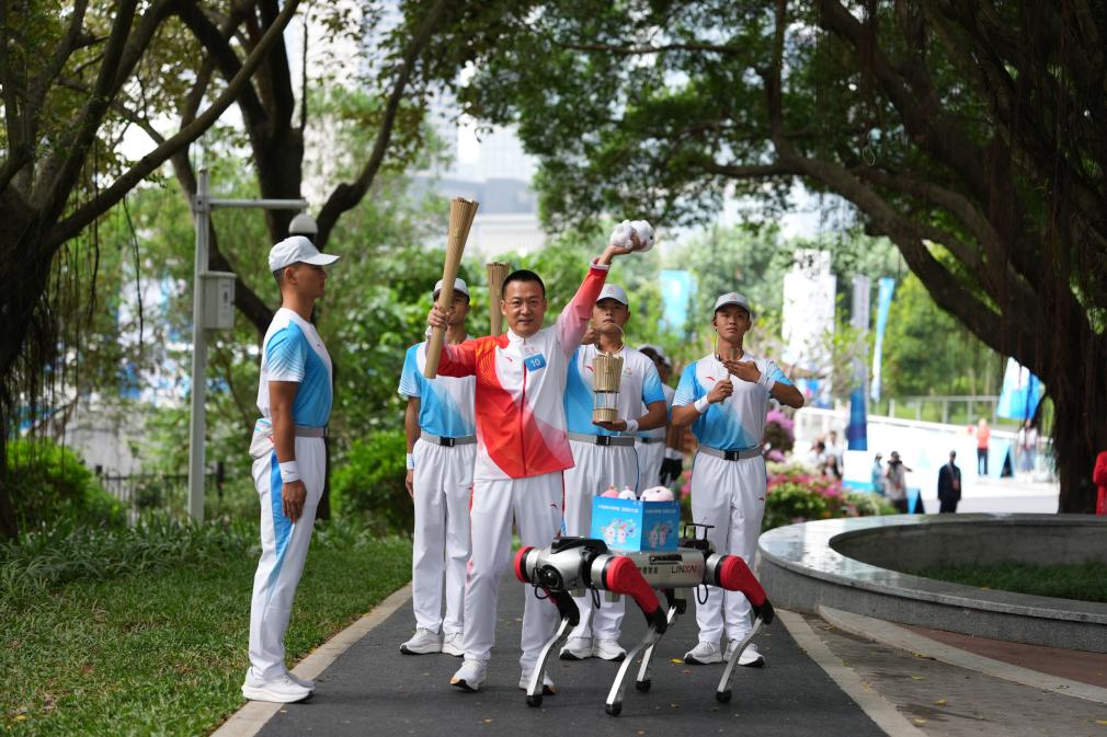 11月2日，火炬手蘭小軍（左二）在火炬傳遞深圳站展示從機器狗上取出的本屆全運會吉祥物玩偶。