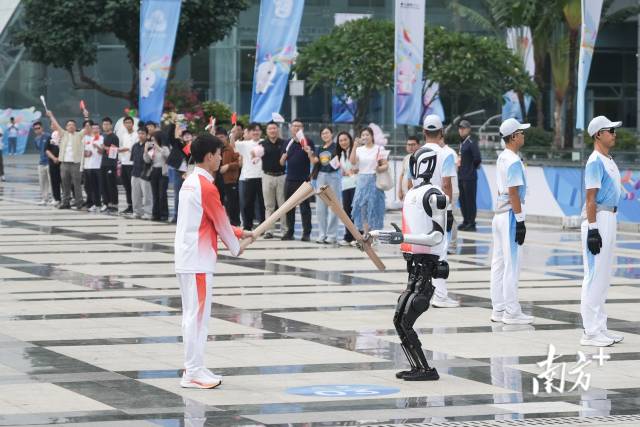 第十五屆全國(guó)運(yùn)動(dòng)會(huì)深圳站火炬?zhèn)鬟f活動(dòng)現(xiàn)場(chǎng)，“0號(hào)”火炬手人形機(jī)器人“夸父”向“手搓火箭”的高中生王裕寧傳遞火炬。